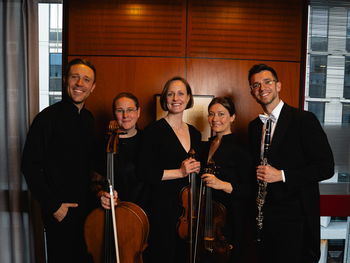 Fem musikere stilt opp foran en brun vegg